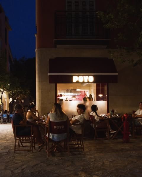 El club de POYO en Palma de Mallorca de noche, con el rótulo iluminado y la terraza ocupada en la plaza.