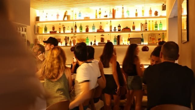 La barra de POYO iluminada por la noche, con la estantería de botellas al fondo y gente de pie tomando algo.